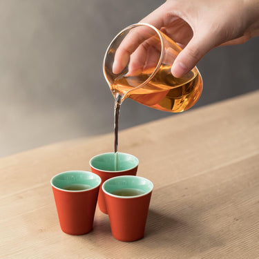 Pouring tea from the glass fair cup into red gongfu tea cups